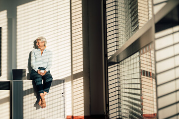 Cheerful business person holding coffee cup sitting by laptop on table in office