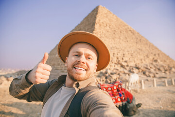 Selfie photo archaeologist man in hat with camel background pyramid of Egyptian Giza, sunset Cairo,...