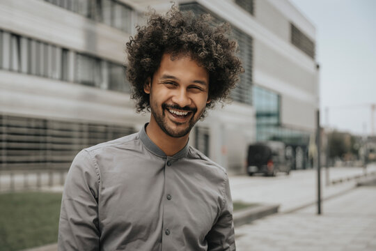 Happy young man with curly hair in front of modern building