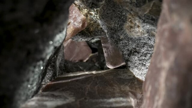 Camera pans inside a pile of gray and brown granite stones against a black background. Rough granite gravel cobblestones with natural texture and fracture patterns. Geology. Stone gorge close up.