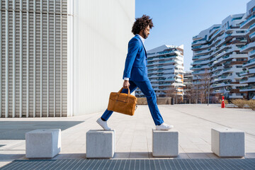 Businessman holding shoulder bag walking on concrete block