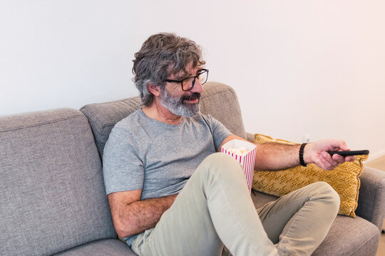 Smiling Man With Popcorn And Remote Control Watching Tv On Sofa At Home