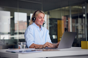 Smiling businesswoman wearing headset using laptop at desk in office