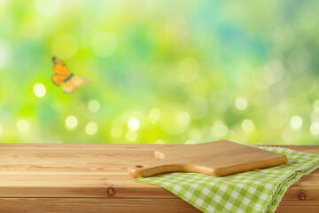 Cutting board and green tablecloth on wooden table over green spring blossom background. Easter...
