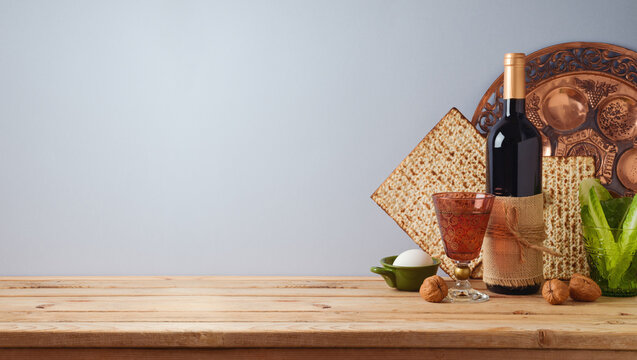 Jewish holiday Passover celebration concept with wine, matzah and seder plate on wooden table over gray background.