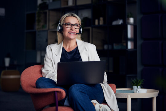 Smiling businesswoman wearing headset working on laptop at office