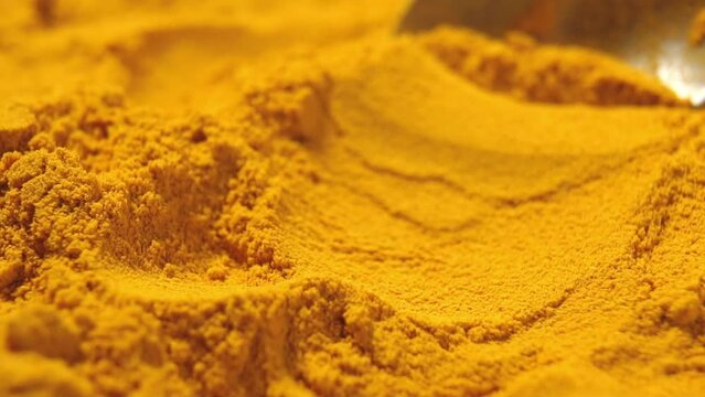 Crumbly crushed turmeric root with spoon. Vegetable condiment. Source of collagen. Yellow seasoning. Movement in slow motion. Macro