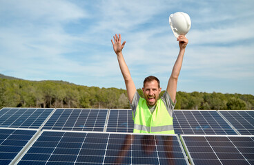 Happy engineer with arms raised amidst solar panels on sunny day