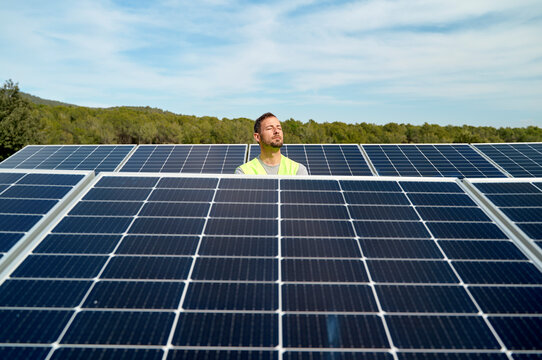 Engineer with eyes closed between solar panels on sunny day