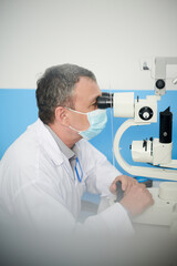 Fototapeta na wymiar Ophthalmologist in protective mask examined eyes of patient with modern autorefractometer