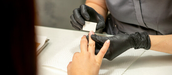 Fototapeta premium Close up of the caucasian hands of a professional manicurist are filing the nails of a young woman. Young caucasian woman receiving a manicure by a beautician with a nail file in a nail salon