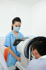 Serious ophthalmic nurse setting refractometer to check eyesight of patient