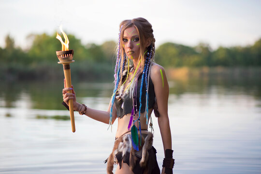 amazon woman with a burning torch in her hands, wearing a medieval fur costume, against the background of the river.
