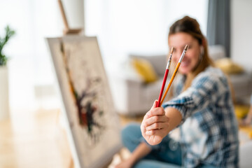 Happy young woman paints on canvas at home