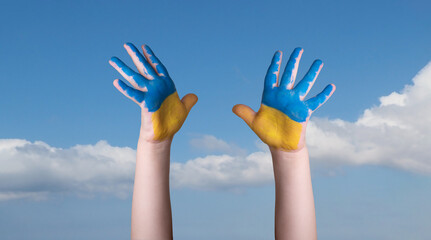 Child's hands painted in the colors of the national flag of Ukraine on blue sky background.