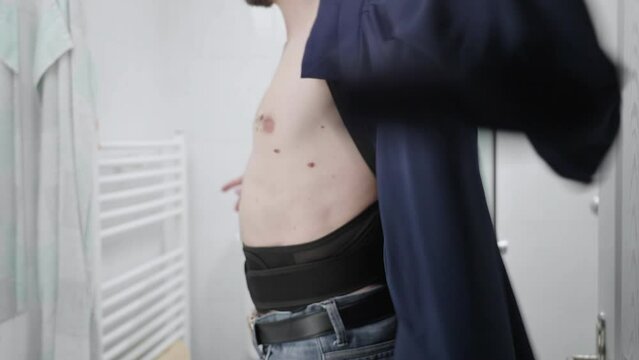 Headless person with orthopedic posture belt under blue shirt on bare skin 4K