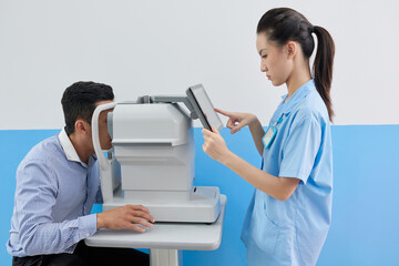 Young female doctor setting refractometer machine to check eyes of patient before vision correction...