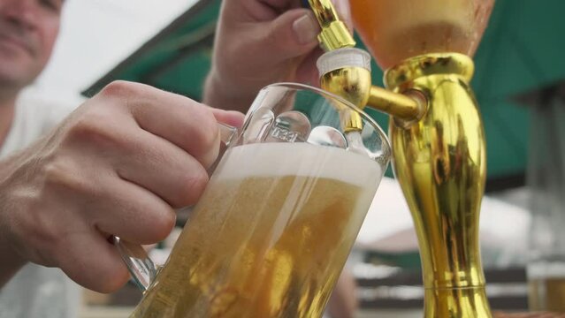 Man pours light beer into glass sitting at table outdoors.