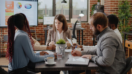Close up of woman presenting marketing project ideas on papers, explaining business plan to coworkers at briefing meeting. People working together to design financial presentation.