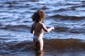 Little curly girl goes swimming alone in the sea