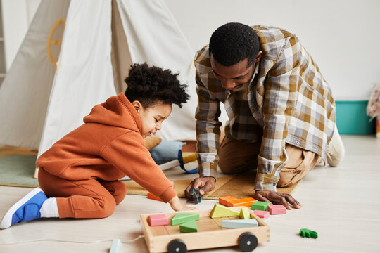 Full length portrait of caring black father playing with son on floor in cozy kids room, fatherhood and family concept