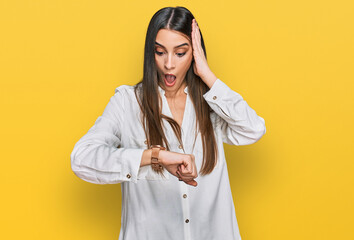 Young beautiful woman wearing casual white shirt looking at the watch time worried, afraid of...