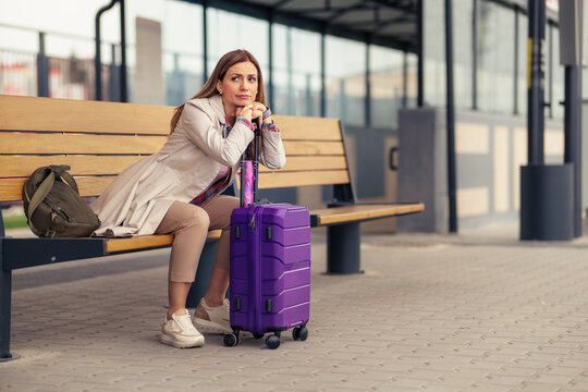 A beautiful woman sits leaning on a suitcase at a train station. She's tired and has a headache.