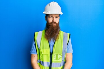 Redhead man with long beard wearing safety helmet and reflective jacket depressed and worry for distress, crying angry and afraid. sad expression.
