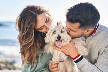 Man and woman holding dog hugging each other kissing at seaside