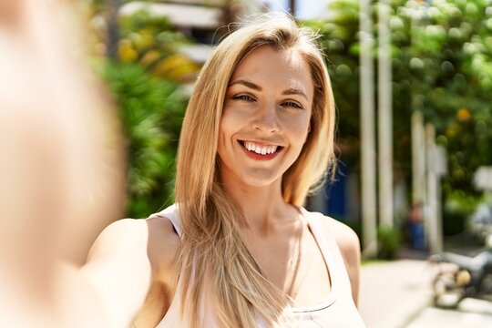 Beautiful blonde woman smiling happy outdoors on a sunny day taking a selfie picture