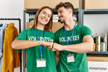 Young hispanic volunteer couple smiling happy bump fists at charity center.