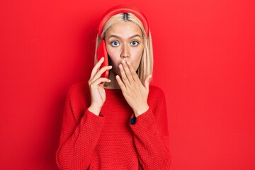 Beautiful blonde woman having conversation talking on the smartphone covering mouth with hand,...