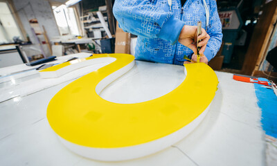 Applying colored yellow membrane to a surface of plastic 3d letter of signboard. worker's hands...