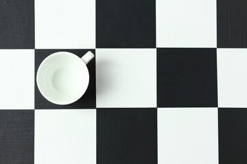 White cup and saucer on a chessboard.