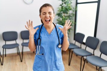 Young brunette doctor woman at waiting room celebrating mad and crazy for success with arms raised...