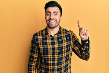 Naklejka premium Young hispanic man wearing casual clothes showing and pointing up with finger number one while smiling confident and happy.