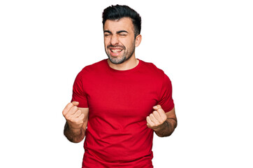 Hispanic man with beard wearing casual red t shirt excited for success with arms raised and eyes closed celebrating victory smiling. winner concept.