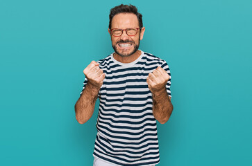 Fototapeta premium Middle age man wearing casual clothes and glasses very happy and excited doing winner gesture with arms raised, smiling and screaming for success. celebration concept.