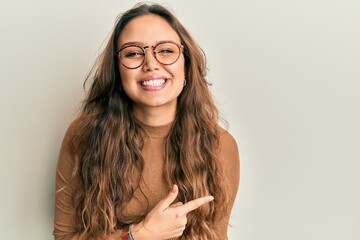 Young hispanic girl wearing casual clothes and glasses cheerful with a smile on face pointing with...