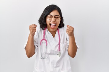 Young hispanic doctor woman wearing stethoscope over isolated background excited for success with...