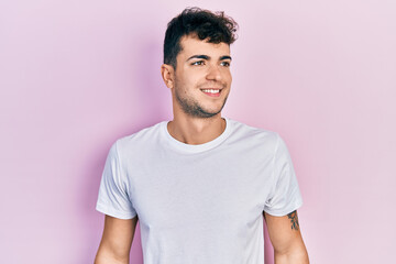 Young hispanic man wearing casual white t shirt looking to side, relax profile pose with natural face and confident smile.