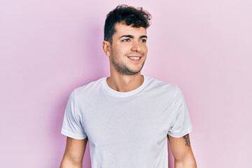 Obraz premium Young hispanic man wearing casual white t shirt looking to side, relax profile pose with natural face and confident smile.