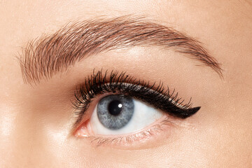 Obraz premium Female blue eye with trendy perfect fashion makeup, eyeliner on eyelid, ideal shaped eyebrow, mascara on eyelashes. Close-up caucasian woman with make up on eyes, skincare cosmetics advertisement.