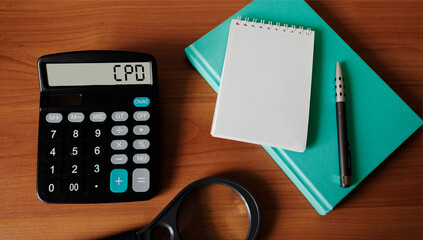 Calculator with CPD text on wooden background with notepad to write