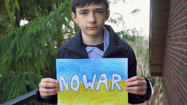 Ukrainian poor boy kid homeless protesting armored conflict holding banner with inscription message text No War on background of yellow blue flag. Crisis, peace, stop aggression in whole world