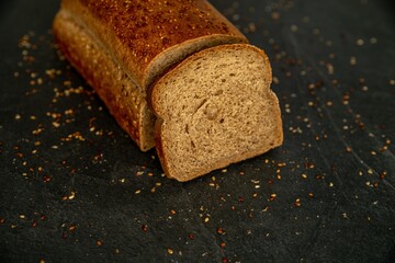 Brick-shaped baked bread with sesame seven on a dark stone background close-up. Cut off piece....