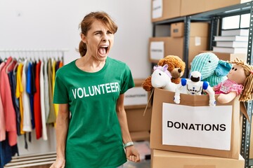 Beautiful caucasian woman wearing volunteer t shirt at donations stand angry and mad screaming...