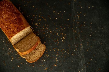 Brick-shaped baked bread with sesame seven on a dark stone background close-up. Cut off piece....