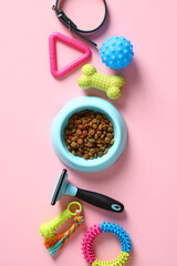 Flat lay composition with bowl of dry feed and pet accessories on pink table.