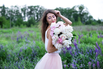 Obraz na płótnie Canvas Beautiful girl with pink peonies, enjoying a bouquet of flowers on background of nature. Happy smiling woman in dress holds peonies in hands. Girl with a bouquet of flowers. Girl in wildflowers. 